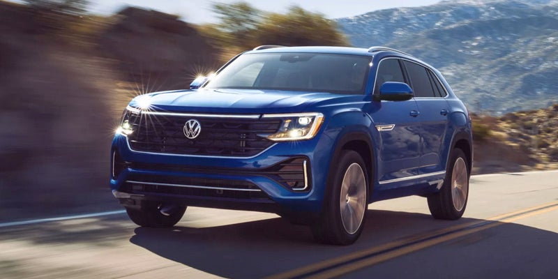 Blue Volkswagen SUV driving on a winding road with mountains in the background under harsh sunlight.