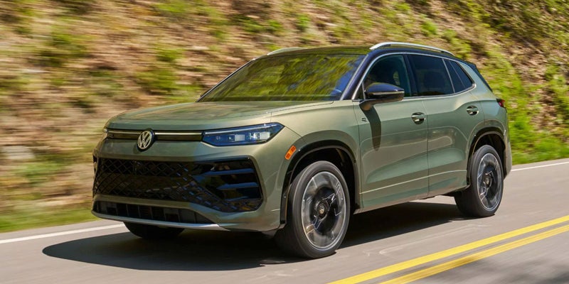 Green Volkswagen Tiguan driving on a two-lane road.