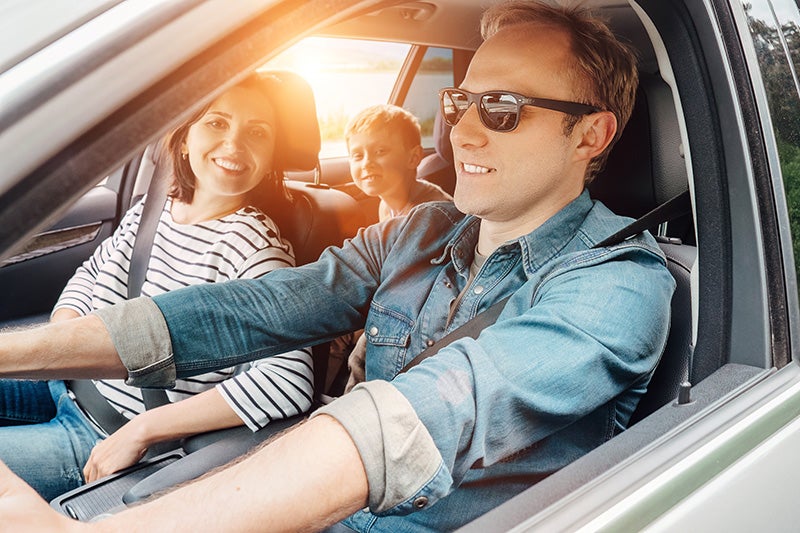 A happy family of three smiles while driving in their car together.