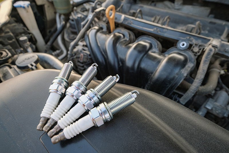 Four new spark plugs lie on a car engine, ready for installation.
